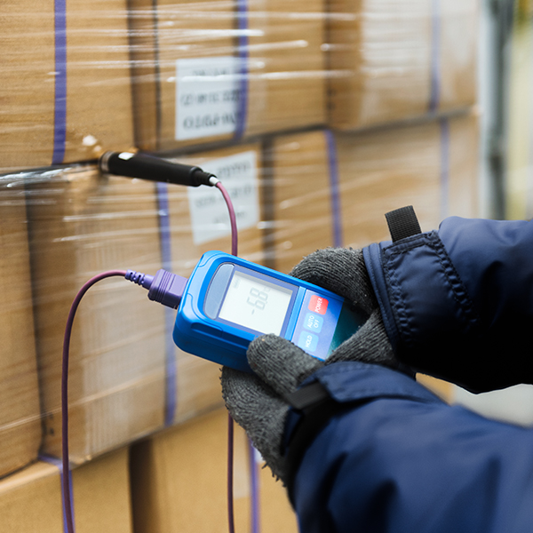 Hand of worker using thermometer to temperature measurement in the goods boxes with ready meals after import in the cold room or warehouse for keep temperature room